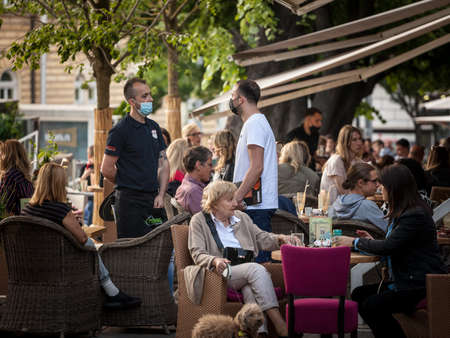 BELGRADE, SERBIA - MAY 29, 2021: Waiter, a server working at the terrace of a cafe serving food to customers wearing a respiratory face mask during the coronavirus covid 19 health crisis.のeditorial素材