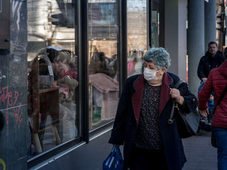 BELGRADE, SERBIA - MARCH 19, 2022: Selective blur on an Old woman looking at prices in window of...