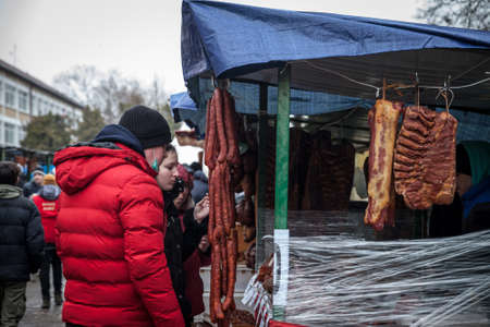 KACAREVO, SERBIA - MARCH 6, 2022: People, customers, tasting smoked and cured meat, mainly sausage, kosasica style, at the stand of a butcher at the Slaninijada Kacarevo market in the serbian countryside.のeditorial素材