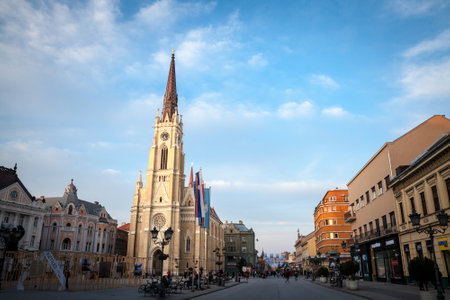 NOVI SAD, SERBIA - MARCH 20, 2022: The Name of Mary Church, or Novi Sad catholic cathedral on a sunny afternoon with a crowd walking on Trg Slobode Square. This cathedral is the landmark of Novi Sad.のeditorial素材