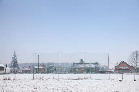 Selective blur on neglected and abandoned Soccer goals with football nets on display on a playground used as a soccer field in Bavaniste, Serbia, covered with snow during a cold winter afternoon.の写真素材