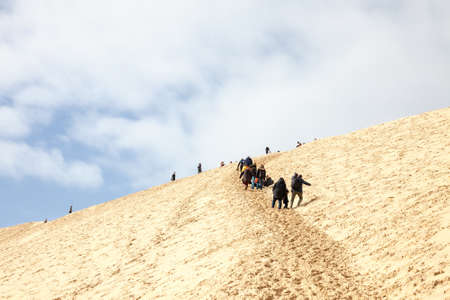 PILAT, FRANCE - FEBRUARY 22, 2022: group of tourists climbing in crowd the sandy slopes of the Pilat Dune (Dune du Pyla). Pilat, or Pyla Dune is the biggest sand dune in Europe, Arcachon Bay, Aquitaine.のeditorial素材