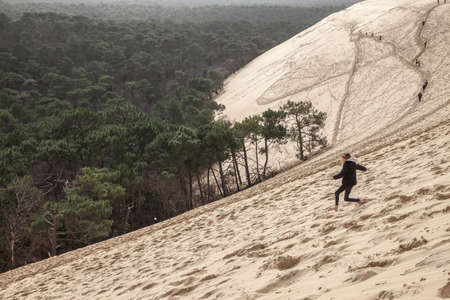 PILAT, FRANCE - FEBRUARY 22, 2022: girl running down the sandy slope of Family of the Pilat Dune (Dune du Pyla). Pilat, or Pyla Dune is the biggest sand dune in Europe, in Arcachon Bay, in Aquitaine.のeditorial素材