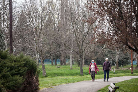 LAZAREVAC, SERBIA - APRIL 11, 2021: Selective blur Two old senior women, friends, wearing a face mask walking respecting social distancing in the streets of Lazarevac on coronavirus covid 19 crisis.のeditorial素材