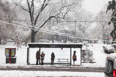 BELGRADE, SERBIA - DECEMBER 12, 2021: Selective blur on a bus stop with people waiting for transportation in a middle of a snowstorm with blurry snow falling in Belgrade.のeditorial素材