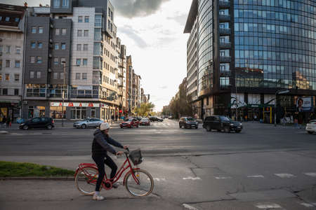 NOVI SAD, SERBIA - APRIL 10, 2022: Young woman, a girl, riding a bicycle in the city center of Novi Sad, Vojvodina, waiting to cross a street with cars at a red traffic light.のeditorial素材