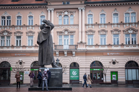 NOVI SAD, SERBIA - APRIL 3, 2022: Svetozar Miletic statue on Trg Slobode Square with a group of youngsters gathering, under the rain, in novi sad, second biggest city of Serbia.のeditorial素材