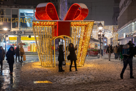 BELGRADE, SERBIA - JANUARY 10, 2022: Girls taking a selfie in front of Giant gift wrap used as the main Christmas decoration on Kneza Mihailova, main street of Belgrade, illuminated for Xmas and the new year.のeditorial素材