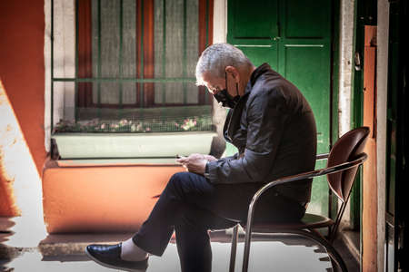 ISTANBUL, TURKEY - MAY 21, 2022: Selective blur on an old senior turkish man sitting and using his mobile phone, a smartphone, to browse the internet in the grand bazaar of istanbul.のeditorial素材
