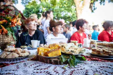 ASANJA, SERBIA - JUNE 19, 2022: Selective blur on portions of Gibanica for sale in Asanja Gibanicijada market with blurred senior women behind. Gibanica is a serbian pastry dish made of cheese.のeditorial素材