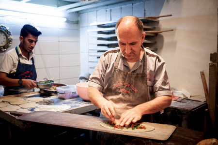 ISTANBUL, TURKEY - MAY 21, 2022: Selective blur on a senior man, a pideci, a baker, preparing a dough for a pide, a typical middle eastern and turkish dish, in a bakery (pide finiri) of istanbul.のeditorial素材