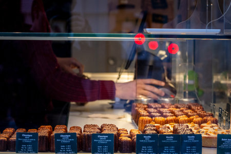 BORDEAUX, FRANCE - FEBRUARY 24, 2022: Selective focus on Canneles Bordelais, a traditional pastry from bordeaux, on a pastry shop, with blurred hand in the back and blurred pastries in front.のeditorial素材
