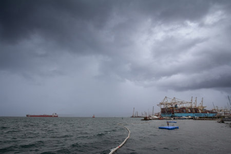 KOPER, SLOVENIA - SEPTEMBER 17, 2021: Young kid swimming in front of a panorama of port of Koper, with container ship and a container terminal. Luka Koper is the main cargo port of Slovenia.のeditorial素材