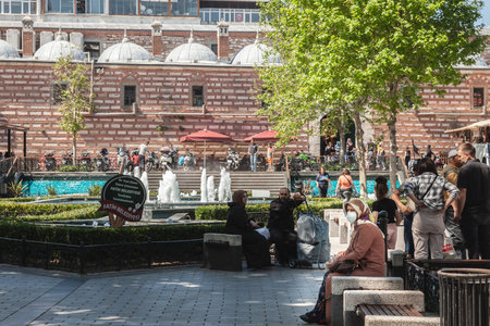 ISTANBUL, TURKEY - MAY 21, 2022: Selective blur on an woman wearing a muslic islamic scarf veil sitting in an istanbul park, wearing a face mask in a crowd during Covid 19 Coronavirus pandemic.のeditorial素材