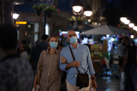 BELGRADE, JANUARY 14, 2021: Selective blur on man and woman, couple, lovers, wearing a facemask, standing in street of Belgrade at night in summer during coronavirus covid 19 health crisis.のeditorial素材
