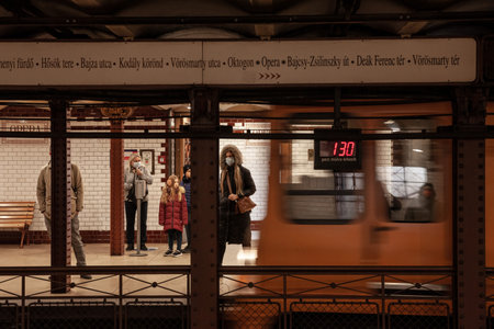 BUDAPEST, HUNGARY - FEBRUARY 27, 2022: Selective blur on people on Budapest metro line 1 at Opera metro station, wearing face mask during covid 19 coronavirus with a metro entering with speed blur.のeditorial素材
