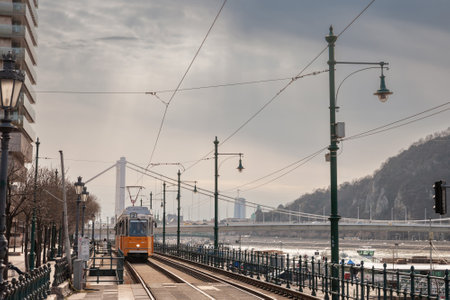BUDAPEST, HUNGARY - FEBRUARY 27, 2022: Budapest tram, or called Villamos, Ganz CSMG, passing in frong of Erzebet Hid Bridge by the danube. Managed by BKK BKV, it is the main public transport network.のeditorial素材