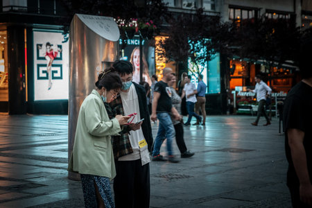 BELGRADE, SERBIA - JUNE 8, 2022: Selective blur on a Young Asian couple, man and woman, Chinese, wearing face mask holding smartphone in the street of Belgrade, on coronavirus covid 19 health crisis.のeditorial素材