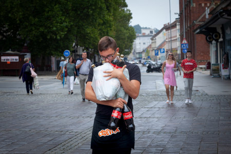 MARIBOR, SLOVENIA - SEPTEMBER 16, 2021: Selective blur on a young man, a waiter, worker, hands full of bottles of coca cola, overloaded, trying to carry them.のeditorial素材