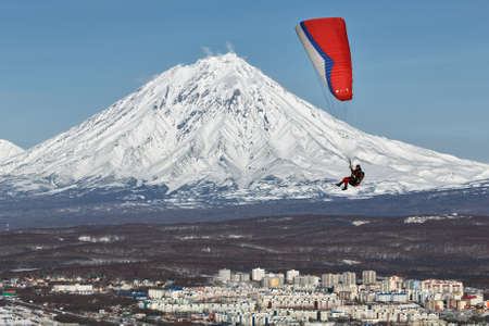 PETROPAVLOVSK-KAMCHATSKY, KAMCHATKA, RUSSIA - NOVEMBER 21, 2014: Paraglider flying over Petropavlovsk-Kamchatsky City on the background of the active Koriaksky Volcano on a sunny day.のeditorial素材