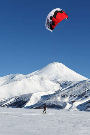 KAMCHATKA, AVACHA VOLCANO, RUSSIA - NOVEMBER 22, 2014: Kiteboarding or Snowkiting - sportsman glides on skis on snow on a background of active Avacha Volcano Avachinsky Volcano on sunny day.のeditorial素材