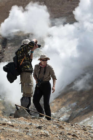 MUTNOVSKY VOLCANO, KAMCHATKA PENINSULA, RUSSIA - JULY 4, 2014: Hiking in Kamchatka - tourists man and woman photographing and looking the steaming smoking fumarole on crater active Mutnovsky Volcano on sunny day.のeditorial素材