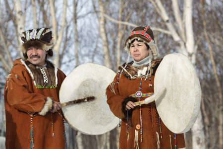 KAMCHATKA, RUSSIA - FEB 5, 2012: Man and woman in the Koryak national dress stand with tambourines in the background of a winter forest. Concert Koryak National Folklore Dance Group. Eurasia, Russian Far East, Kamchatka Region.のeditorial素材