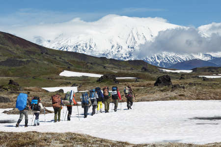 Hiking on Kamchatka: group of hiker with backpack goes in mountain on background of beautiful Klyuchevskaya Group of Volcanoes on sunny day. Kamchatka Peninsula, Russian Far East, Eurasia.の写真素材