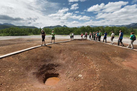 NALYCHEVO, KAMCHATKA, RUSSIA - JULY 30, 2014: Tourists walk on wooden deck, overlooking Thermal Pad Boiler, or Travertine Shield Boiler, with sleep and active griffins (mud pot) with thermal water.のeditorial素材