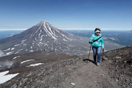 AVACHA VOLCANO, KAMCHATKA PENINSULA, RUSSIA - AUGUST 07, 2014: Hiking on Kamchatka - woman tourist climbing to top of Avachinsky Volcano on background of Koryaksky Volcano in sunny weather.のeditorial素材