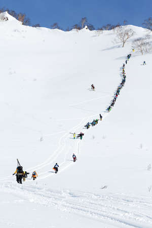 KAMCHATKA PENINSULA, RUSSIA - MARCH 9, 2014: Large group of sportsmens - skiers and snowboarders climbing the steep mountain for freeride. Competition Kamchatka Freeride Open Cup on Russian Far East.のeditorial素材