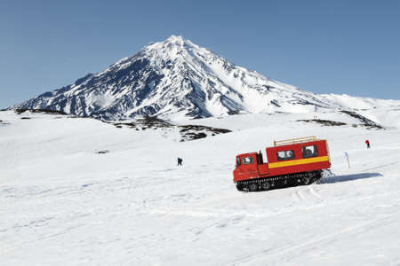 KORYAK VOLCANO, KAMCHATKA PENINSULA, RUSSIA - APRIL 26, 2014: Snowcat driving with sportsman on board (skiers and snowboarders) on snowy slopes of mountains on background of active Koryak Volcano.のeditorial素材