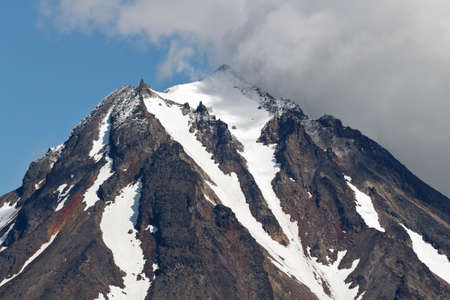 Mountainous landscape of Kamchatka Peninsula: view of top of rocky cone of Vilyuchinsky Volcano, mountain peak and steep slope of volcano with snowfield, glaciers. Russian Far East, Kamchatka Region.の写真素材