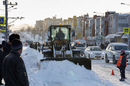 PETROPAVLOVSK KAMCHATSKY CITY, KAMCHATKA PENINSULA, RUSSIAN FAR EAST - DEC 27, 2017: Front end wheel loader cleans after winter snowstorm (blizzards) main road in Petropavlovsk City (sun back light).のeditorial素材