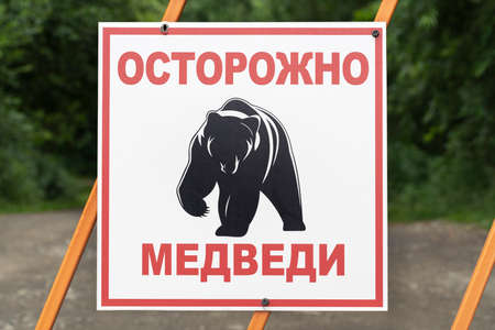 KAMCHATKA PENINSULA, RUSSIAN FAR EAST - AUGUST 4, 2018: Warning sign on fence in Russian: Caution bears and black pictogram Kamchatka brown bear. Sign on background of green forest and country road.のeditorial素材