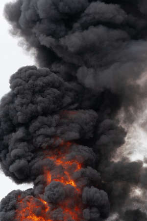 Flames of red-orange fire, motion clouds of black smoke covered sky. Selective focus, motion blur, haze from strong fire and high temperature from flames.の写真素材