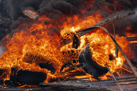 Burning automobile tires, strong flame of red fire and clouds of black fumes in sky. Selective focus, blur from strong fire.の写真素材