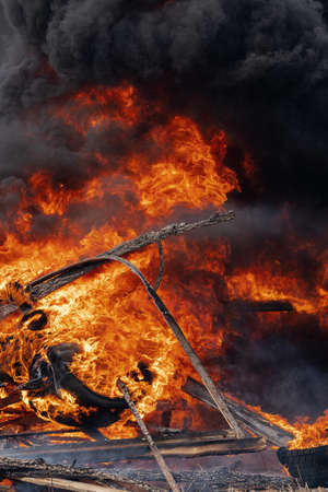 Burning automobile wheels, strong flame of red fire and clouds of black fumes in sky. Selective focus, blur from strong fire.の写真素材