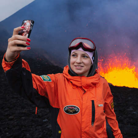 KAMCHATKA PENINSULA, RUSSIA - JULY 27, 2013: Eruption Tolbachik Volcano on Kamchatka, young girl hipster traveler photographed selfie on background lava lake erupting in crater of active volcano.のeditorial素材