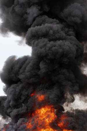 Huge flames of red fire and motion clouds of black smoke covered sky. Selective focus, motion blur from strong fire and high temperature from flames.の写真素材