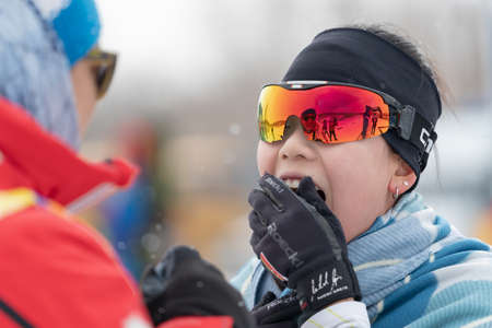 Sportswoman biathlete Lee Hyunju (South Korea) shows at finish delight to coach after rifle shooting and skiing. Open regional youth biathlon competitions East Cup. Kamchatka, Russia - Apr 12, 2019.のeditorial素材