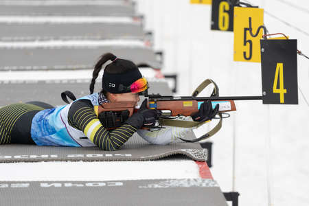 Sportswoman biathlete Lee Hyunju (South Korea) rifle shooting in prone position. Biathlete in shooting range of Open regional youth biathlon competitions East Cup. Kamchatka, Russia - Apr 12, 2019のeditorial素材