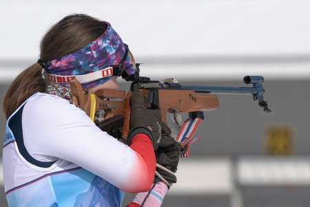 Sportswoman biathlete aiming, rifle shooting standing position. Kamchatka biathlete Maria Babkina in shooting range. Junior biathlon competitions East Cup. Kamchatka Peninsula, Russia - April 13, 2019のeditorial素材