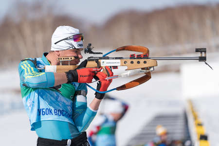 Sportsman biathlete aiming rifle shooting in standing position. Kazakhstan biathlete Kireyev Vladislav in shooting range Junior biathlon competitions East of Cup. Kamchatka, Russia - April 14, 2019のeditorial素材