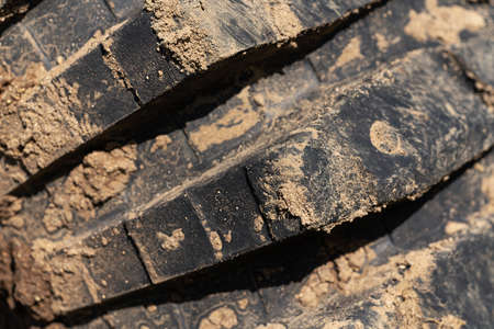 Close-up of old used rubber mud terrain tire with worn wear-resistant tread. Black muddy off-road...