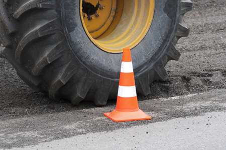 Yellow wheel with pneumatic tire produced by Petlas - Turkish tyre company. Wheel on road reclaimer Caterpillar during road restoration, traffic road cone on asphalt. Kamchatka, Russia - Aug 27, 2019.のeditorial素材