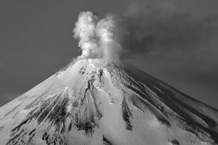 Winter Volcano Avachinskaya Sopka - active mount of Kamchatka Peninsula, volcanic activity of Avacha Volcano: steam, gas, ashes erupting from crater in sky. Dramatic clouds moody black and white imageの写真素材