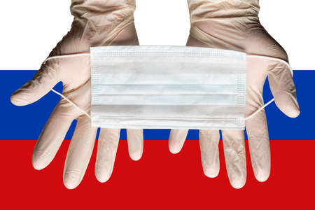 Nurse holding respiratory face mask in hands in white gloves on background flag of Russian Federation. Concept coronavirus quarantine, pandemic outbreak, grippe. Medical respiratory bandage for face.の写真素材