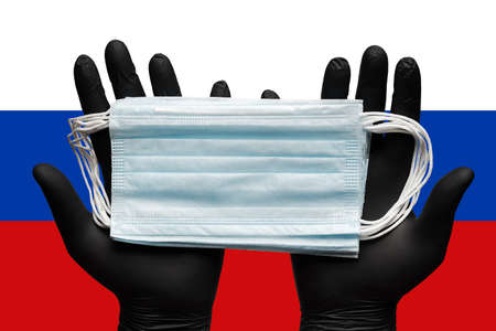 Doctor holding respiratory face mask in hands in blue gloves on background flag of Russia. Concept...
