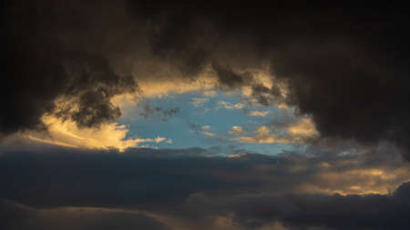 Dramatic clouds illuminated rising of sun floating in sky. Natural weather, meteorology background. Heavenly landscape image ready for design, replace sky in photo editor. Blurred motion, soft focus.の写真素材